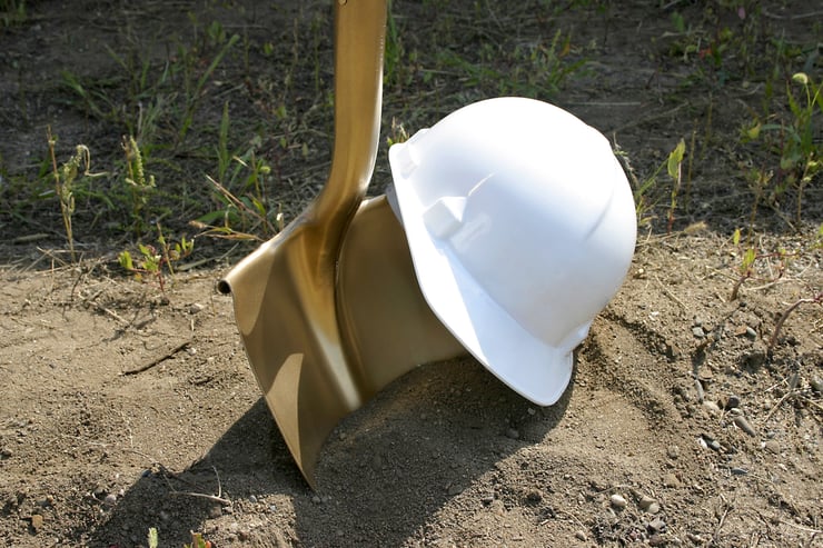 Shovel in dirt with a construction helmet on top. 